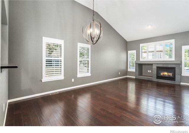 unfurnished living room with a fireplace, wood-type flooring, high vaulted ceiling, and an inviting chandelier