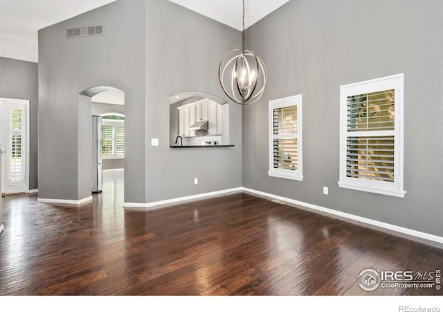 unfurnished living room featuring an inviting chandelier, high vaulted ceiling, wood-type flooring, and a wealth of natural light