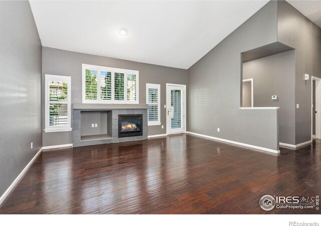 unfurnished living room featuring a tiled fireplace, hardwood / wood-style floors, and high vaulted ceiling