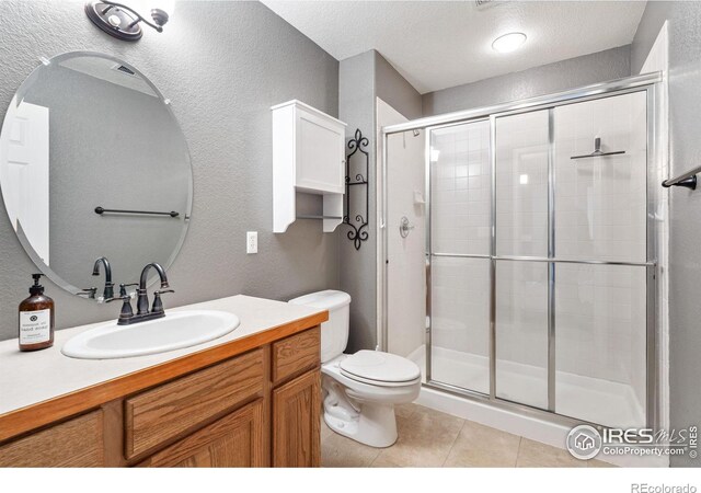 bathroom featuring tile patterned flooring, walk in shower, a textured ceiling, toilet, and vanity