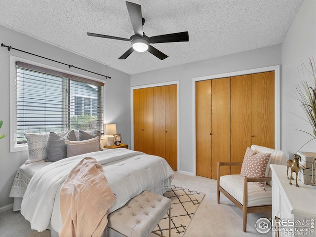 carpeted bedroom with multiple closets, ceiling fan, and a textured ceiling