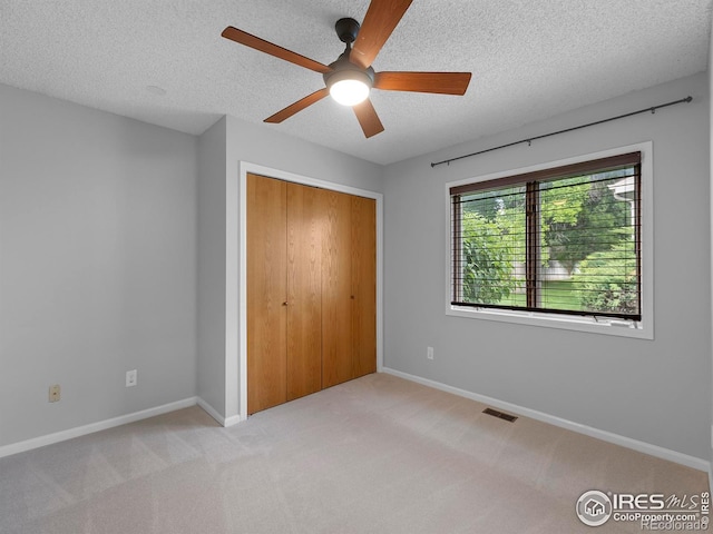 unfurnished bedroom featuring ceiling fan, light colored carpet, a closet, and a textured ceiling