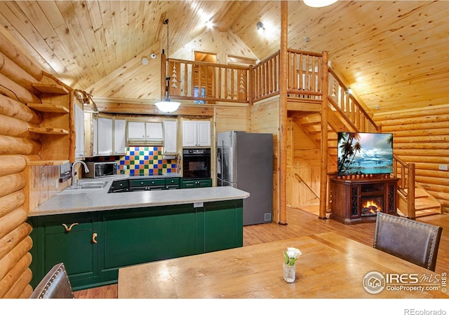 kitchen with appliances with stainless steel finishes, kitchen peninsula, log walls, and high vaulted ceiling