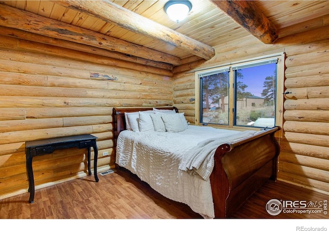 bedroom with beam ceiling, hardwood / wood-style flooring, log walls, and wooden ceiling