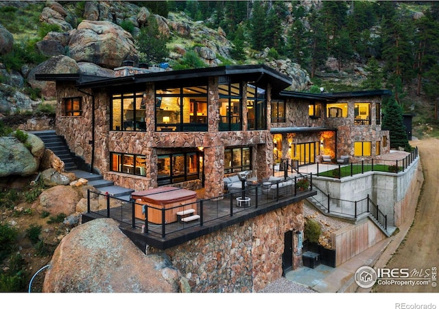 back of property with stone siding, a patio area, stairway, and an outdoor living space with a fireplace