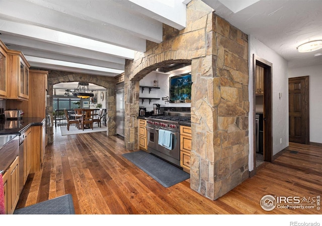 kitchen featuring arched walkways, premium appliances, dark countertops, and glass insert cabinets