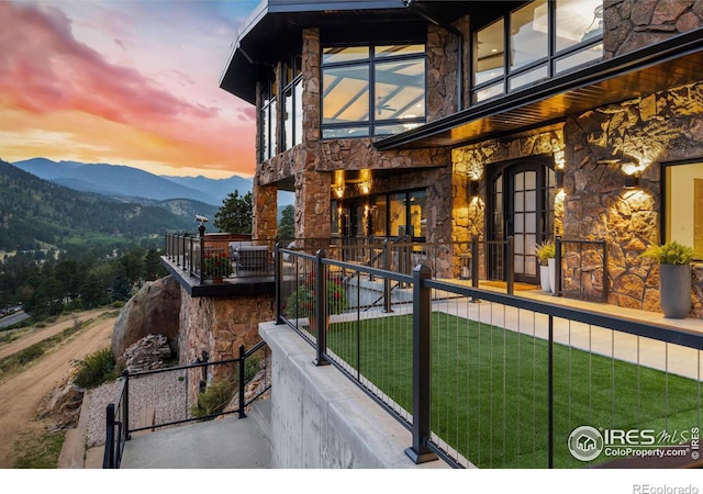 property exterior at dusk with a lawn, a mountain view, and a balcony