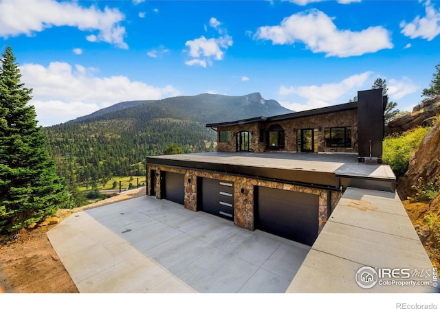 view of front of property with a garage, stone siding, a mountain view, and a wooded view