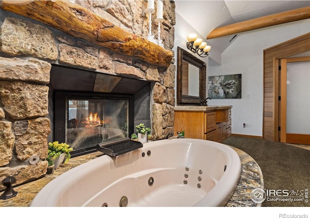 bathroom featuring a fireplace, vaulted ceiling, vanity, a whirlpool tub, and baseboards