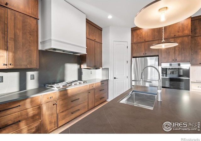 kitchen with sink, custom exhaust hood, tasteful backsplash, stainless steel counters, and appliances with stainless steel finishes