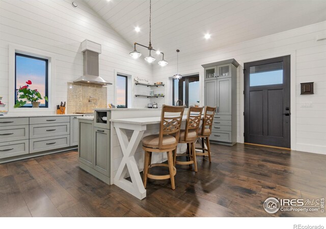 kitchen with dark wood-type flooring, gray cabinetry, hanging light fixtures, and wall chimney range hood