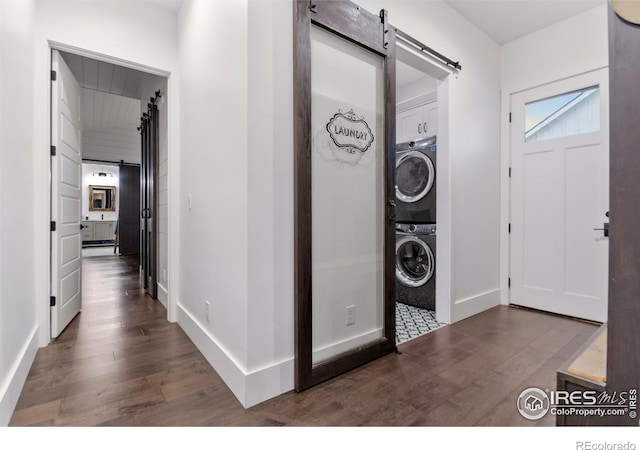 clothes washing area featuring dark hardwood / wood-style flooring, a barn door, and stacked washer / drying machine