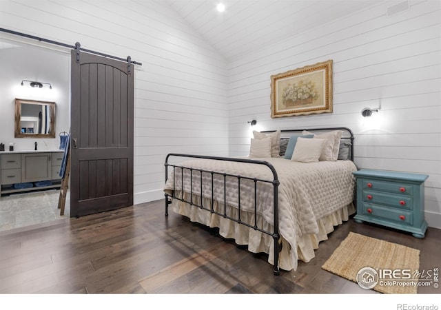 bedroom with wood walls, a barn door, hardwood / wood-style flooring, vaulted ceiling, and sink