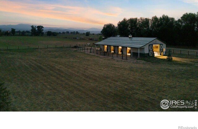 yard at dusk with a mountain view, an outbuilding, and a rural view