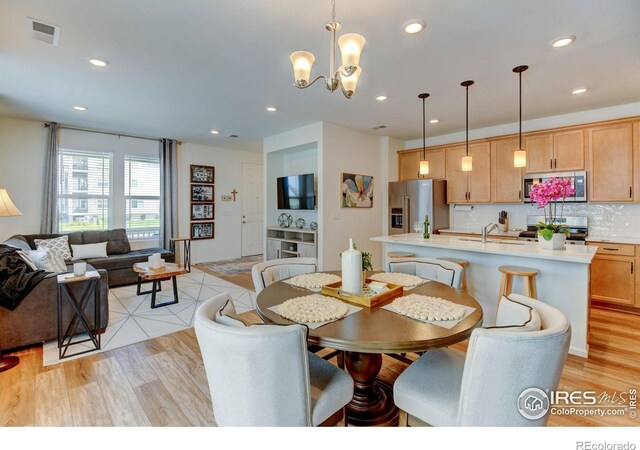 dining space with sink, light wood-type flooring, and a notable chandelier