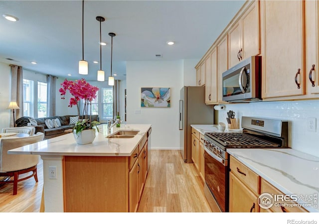 kitchen with sink, stainless steel appliances, a center island with sink, decorative light fixtures, and light wood-type flooring