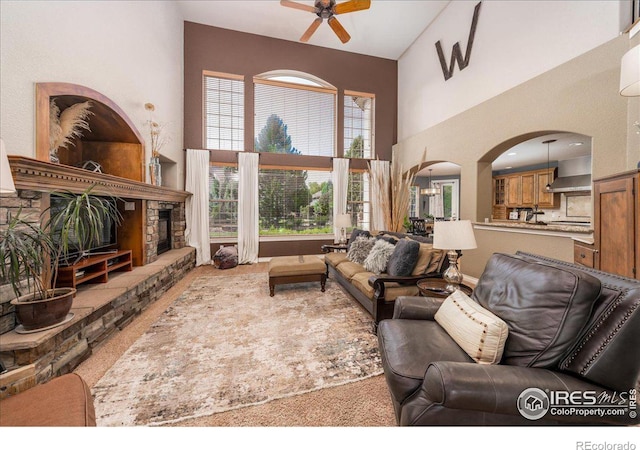 living room with a fireplace, a towering ceiling, carpet, and ceiling fan