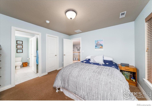 bedroom featuring light carpet, ensuite bath, and a textured ceiling