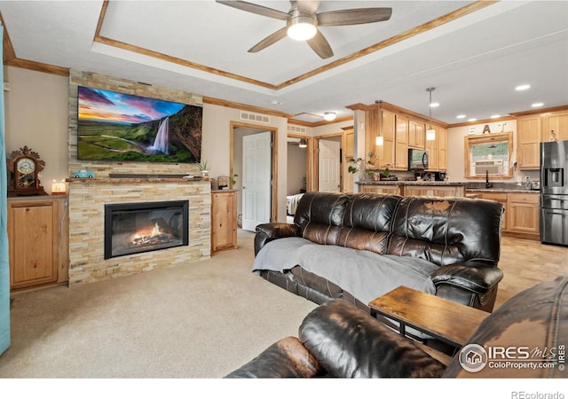 carpeted living room featuring a fireplace, a tray ceiling, crown molding, and ceiling fan