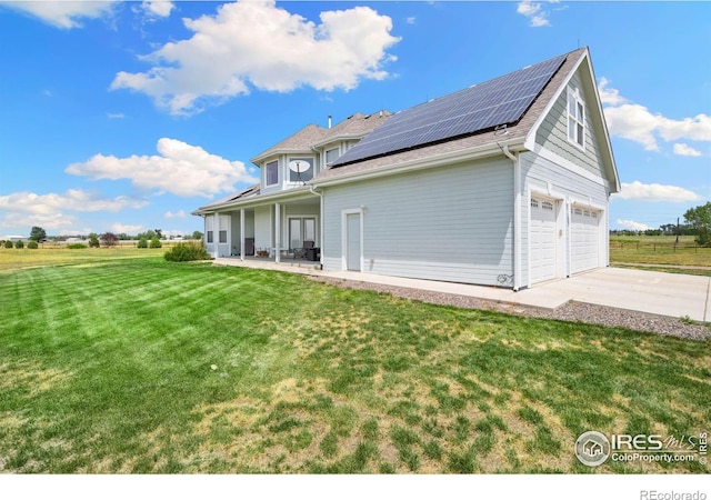 rear view of house with a garage, a yard, and solar panels