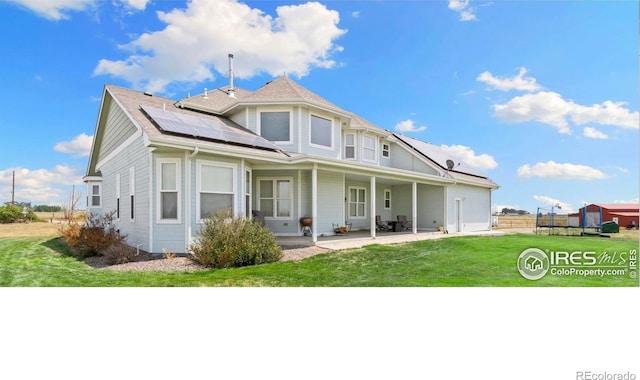 rear view of property featuring a patio, a yard, and solar panels