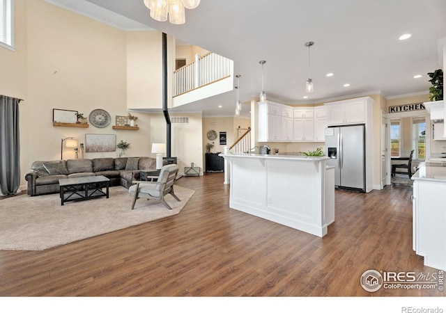 kitchen with white cabinetry, hanging light fixtures, ornamental molding, stainless steel fridge, and dark wood-type flooring