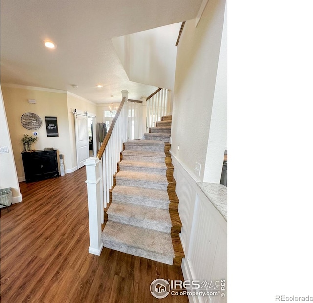 stairway with crown molding, dark hardwood / wood-style flooring, a barn door, and an inviting chandelier