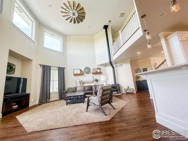 living room with a high ceiling, crown molding, dark hardwood / wood-style floors, and a wood stove