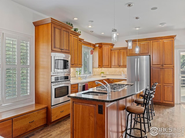 kitchen with tasteful backsplash, decorative light fixtures, a center island with sink, light hardwood / wood-style flooring, and appliances with stainless steel finishes