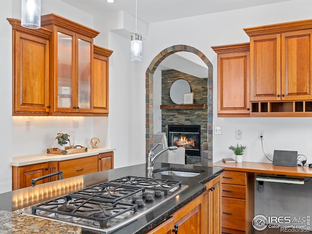 kitchen featuring a fireplace, stainless steel gas stovetop, sink, dark stone counters, and hanging light fixtures