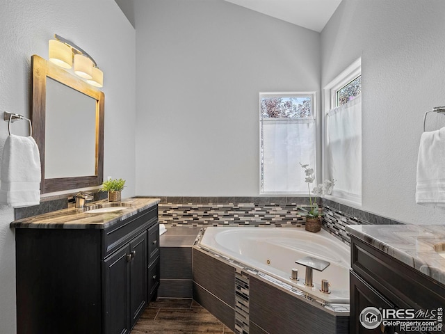 bathroom with hardwood / wood-style floors, vanity, and a relaxing tiled tub