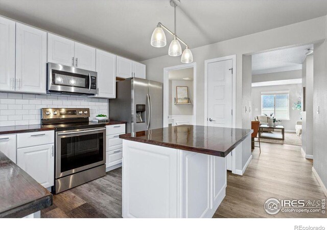 kitchen with appliances with stainless steel finishes, tasteful backsplash, hardwood / wood-style floors, and white cabinetry