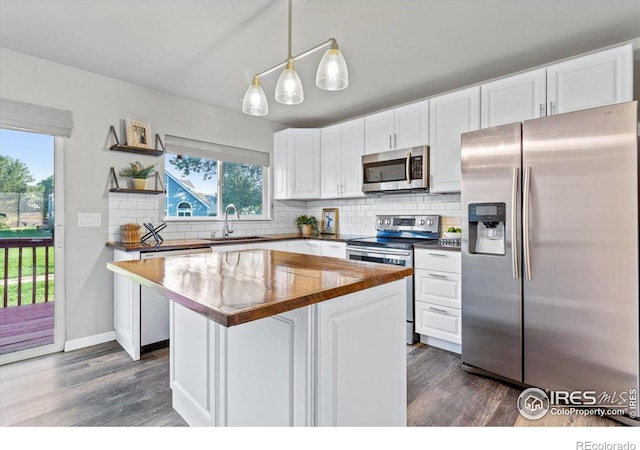 kitchen featuring appliances with stainless steel finishes, white cabinetry, hanging light fixtures, backsplash, and a kitchen island