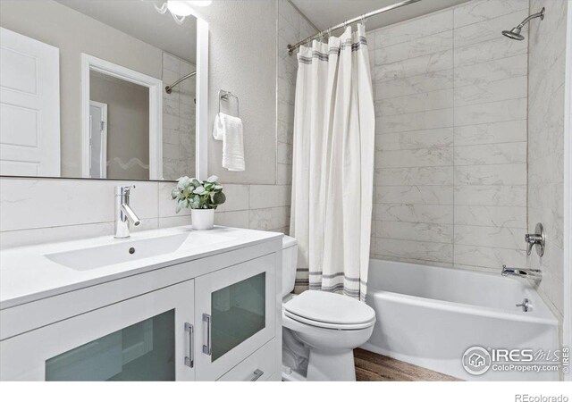 full bathroom with shower / bathtub combination with curtain, tile walls, vanity, wood-type flooring, and toilet