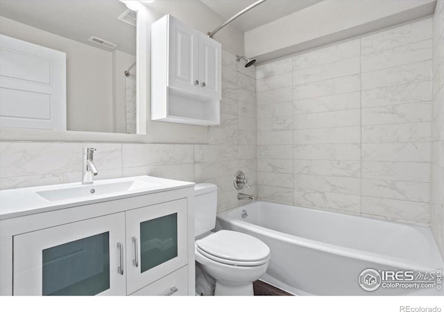 full bathroom with tile walls, backsplash, tiled shower / bath combo, vanity, and toilet