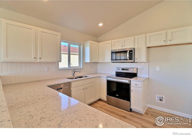 kitchen with lofted ceiling, white cabinets, sink, light stone counters, and stainless steel appliances