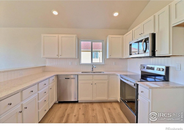 kitchen with stainless steel appliances, vaulted ceiling, sink, white cabinets, and light hardwood / wood-style floors