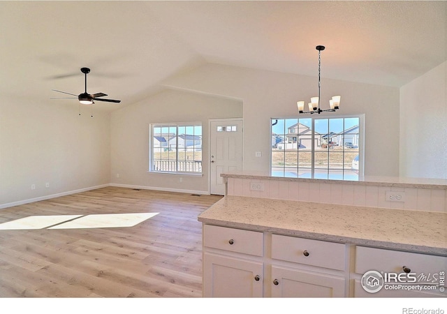 kitchen featuring lofted ceiling, white cabinets, light stone countertops, light wood-type flooring, and decorative light fixtures