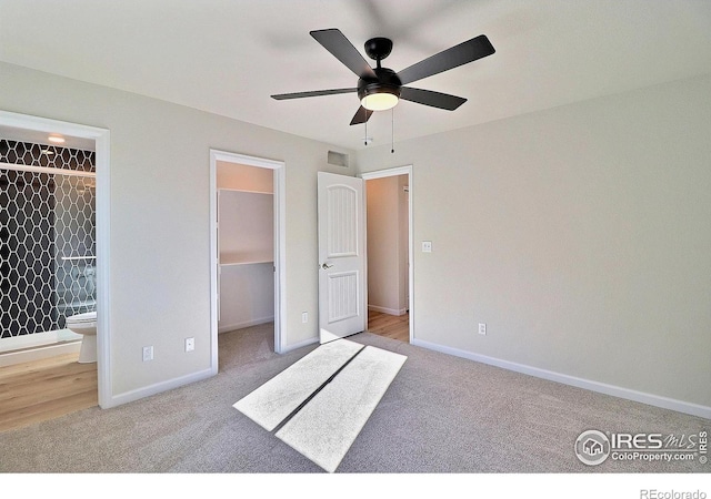 unfurnished bedroom featuring light carpet, ensuite bath, ceiling fan, a spacious closet, and a closet