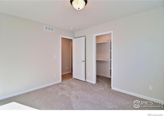 unfurnished bedroom with a walk in closet, light colored carpet, and a closet