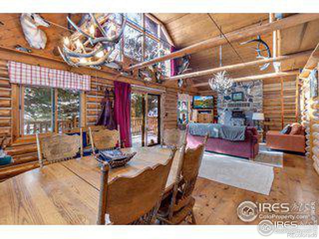 dining space featuring log walls, wooden ceiling, hardwood / wood-style flooring, a stone fireplace, and vaulted ceiling