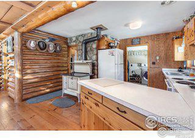 kitchen with hardwood / wood-style floors, log walls, wood walls, and white refrigerator