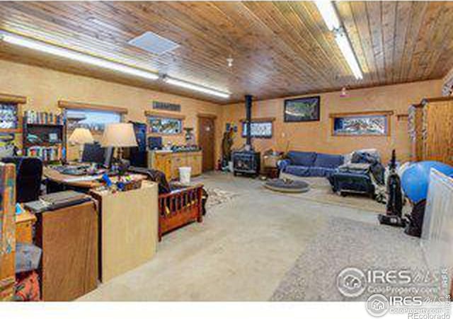 carpeted living room featuring a wood stove and wood ceiling