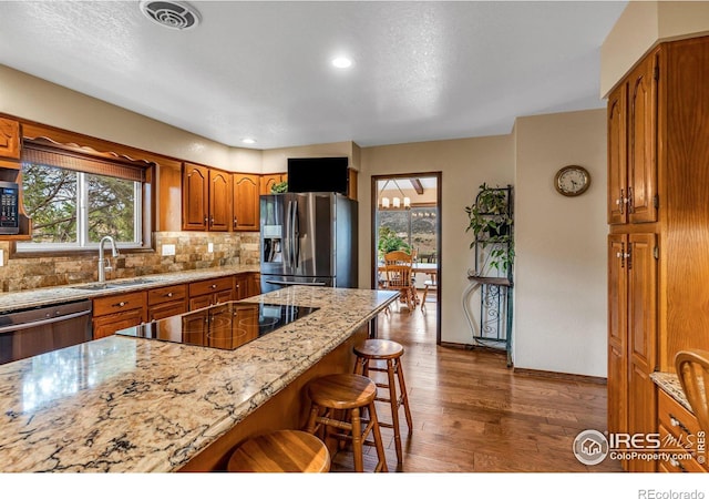 kitchen with black appliances, wood-type flooring, a breakfast bar area, light stone counters, and backsplash