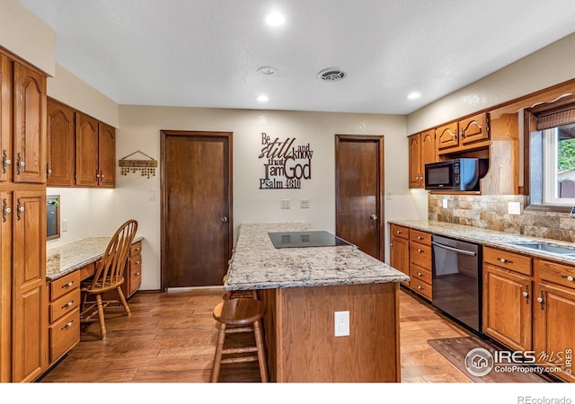 kitchen with a kitchen bar, light stone counters, light wood-type flooring, and black appliances