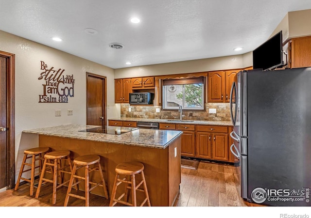 kitchen with light hardwood / wood-style floors, black appliances, a breakfast bar, and tasteful backsplash