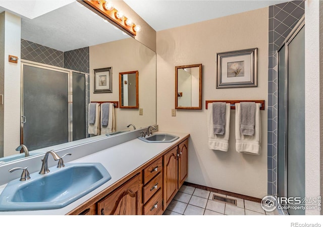 bathroom with a shower with shower door, tile patterned floors, and dual bowl vanity