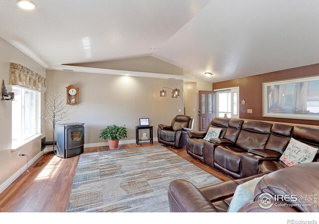 living room featuring plenty of natural light, light hardwood / wood-style floors, a wood stove, and vaulted ceiling