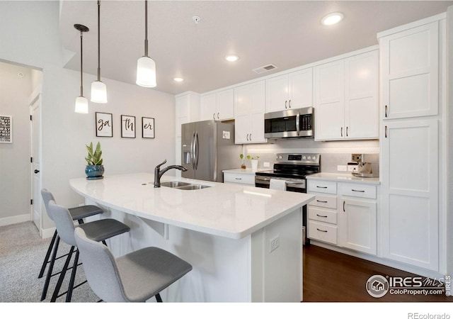 kitchen with appliances with stainless steel finishes, sink, decorative light fixtures, white cabinetry, and a breakfast bar area