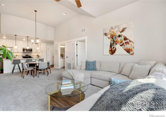 carpeted living room with ceiling fan and high vaulted ceiling